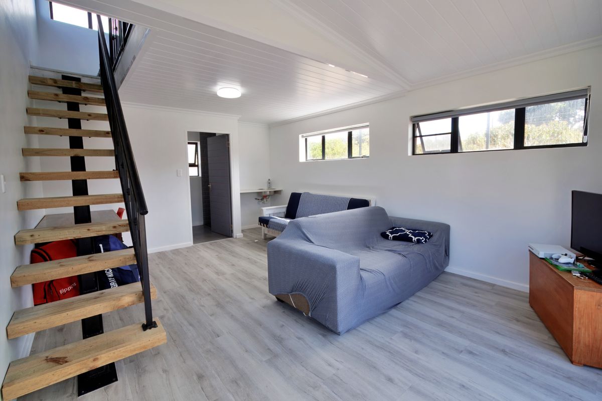 Open-plan living area featuring modern laminate flooring, a timber staircase with metal railing, and a tongue and groove ceiling.