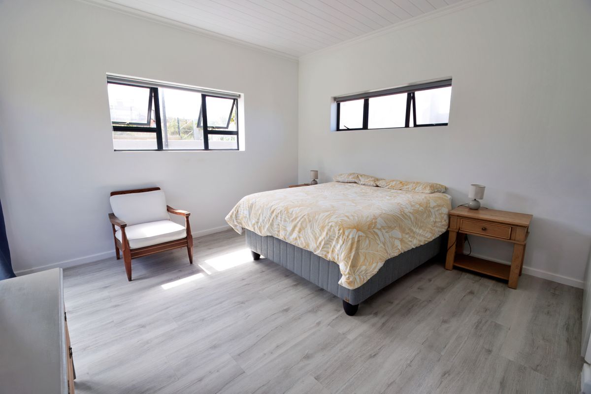 A bright and spacious bedroom featuring modern timber-look laminate flooring, horizontal awning windows, and a clean, neutral aesthetic.