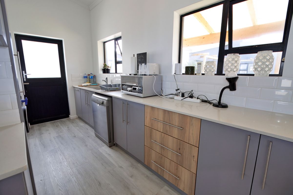 Modern kitchen featuring two-tone cabinetry, quartz countertops, subway tile backsplash, stainless steel dishwasher, and durable laminate flooring with direct access to the exterior.