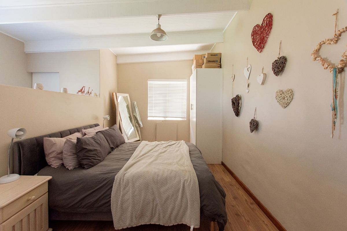 A cozy bedroom featuring laminate flooring, exposed beam ceilings, and natural light through a window with venetian blinds.
