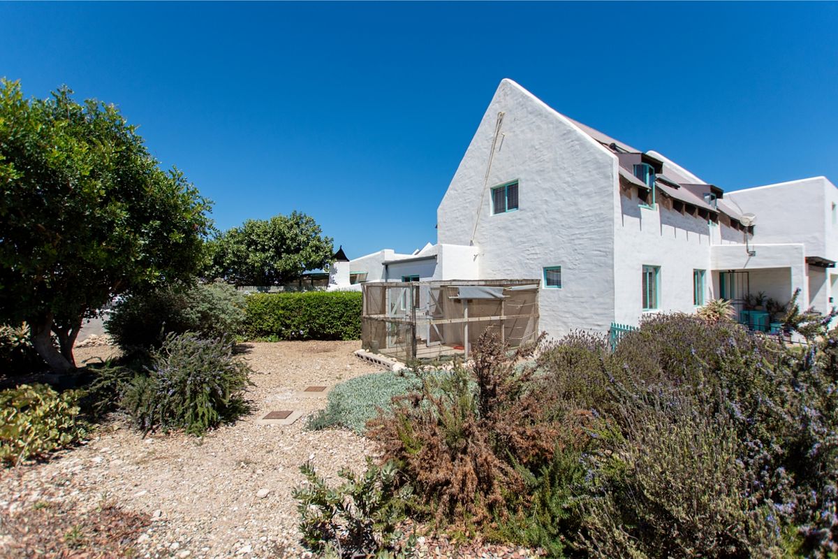 A view of the rear elevation of the white-walled house, featuring a well-established garden with gravel pathways and mature landscaping.