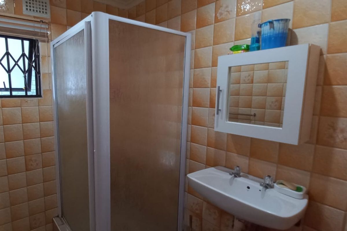 A functional bathroom featuring a shower enclosure, wall-mounted basin, and medicine cabinet, finished with dated ceramic wall tiles.