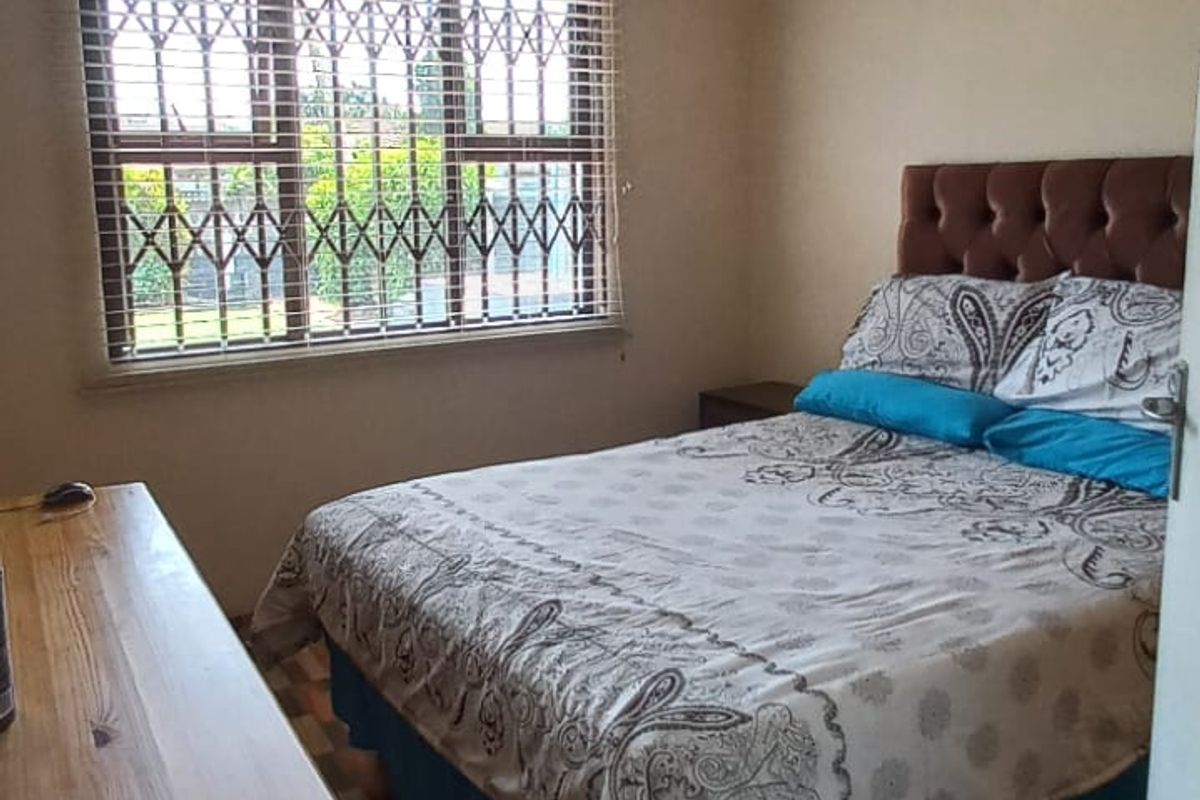 A bedroom featuring tiled flooring, an air conditioning unit, and a window fitted with a security gate and venetian blinds.