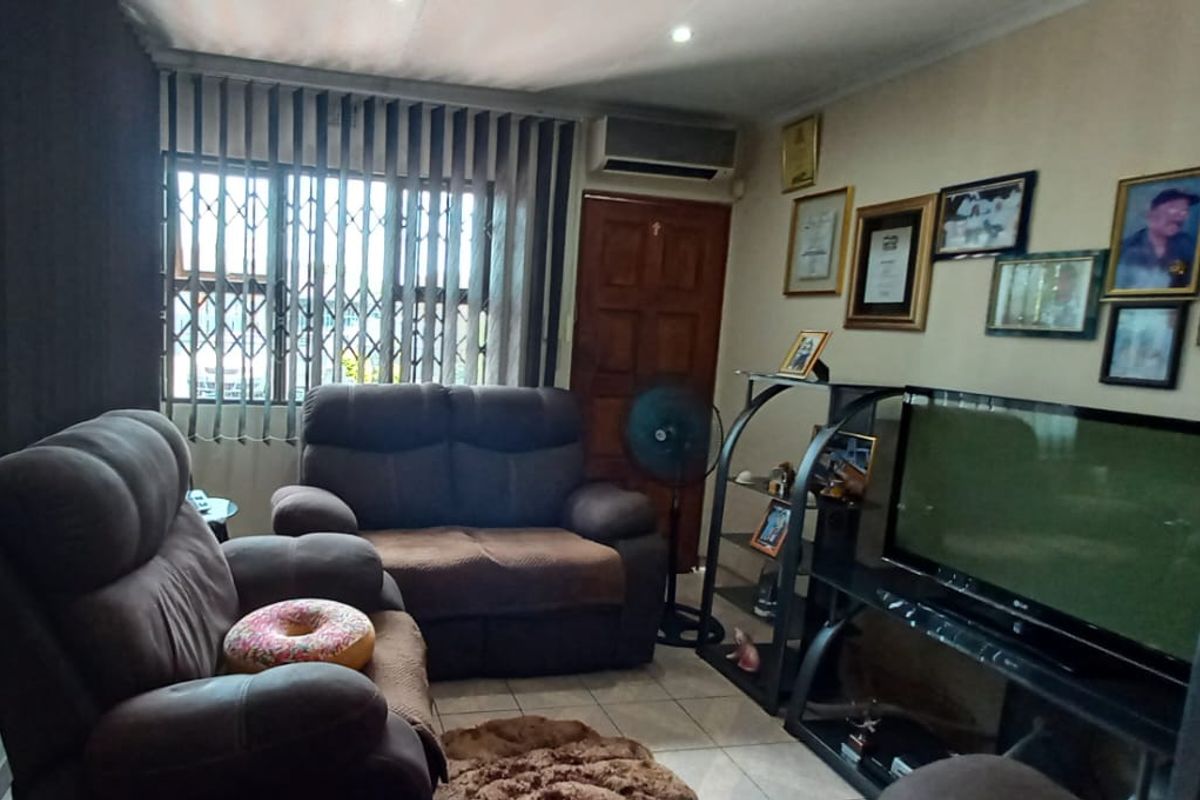 A living room featuring tiled flooring, an air conditioning unit, and a window fitted with security bars and vertical blinds.