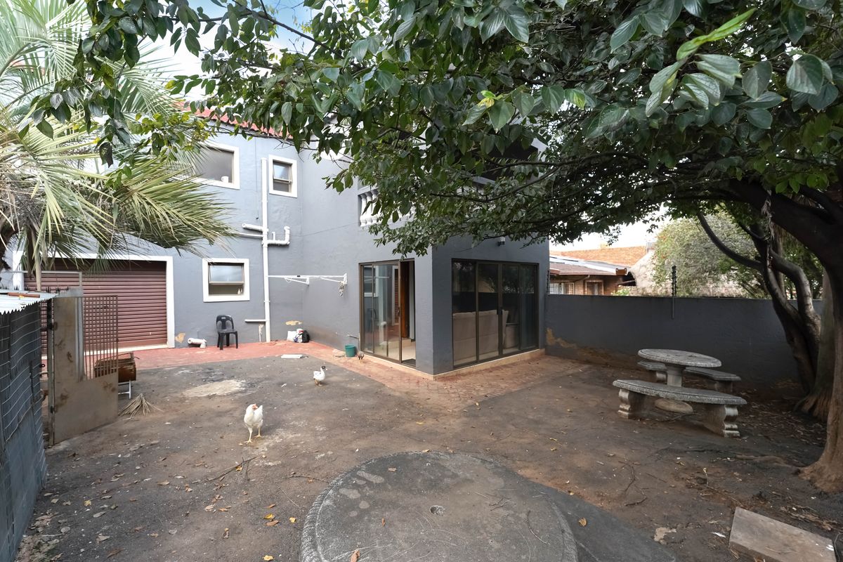 Rear exterior view of the property featuring a paved courtyard area, dark grey rendered walls, and sliding glass doors leading into the home.