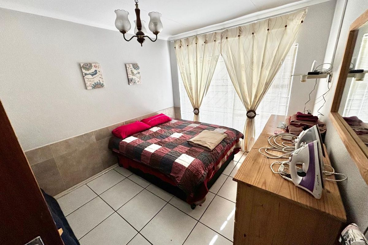 A bedroom featuring tiled flooring, a ceiling-mounted light fixture, and large windows with curtains, providing a functional living space.