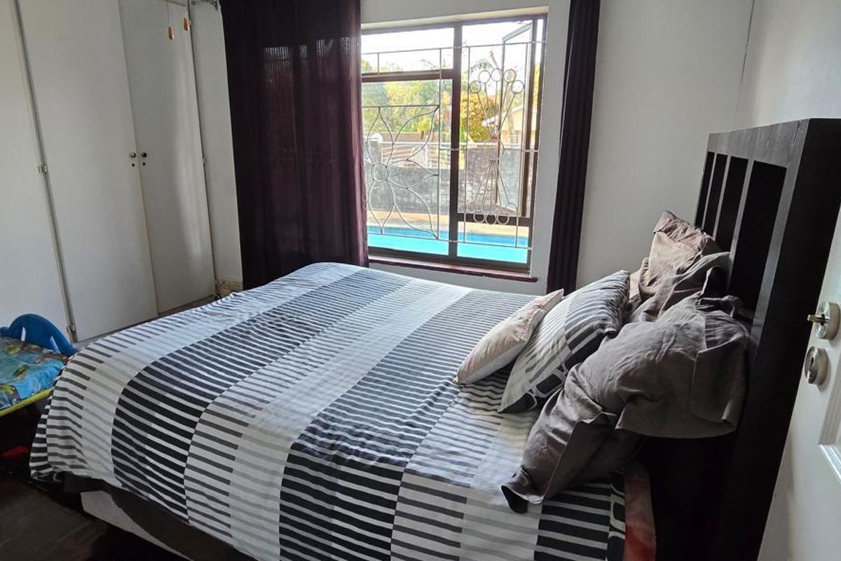 A bedroom featuring built-in cupboards, dark wood-toned flooring, and a window view overlooking the swimming pool area.