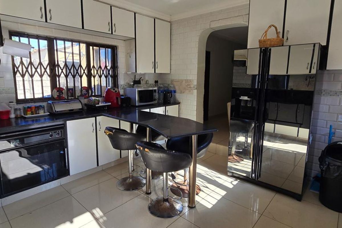 A functional kitchen featuring white cabinetry with black trim, dark countertops, a built-in oven, gas hob, and a breakfast bar area.
