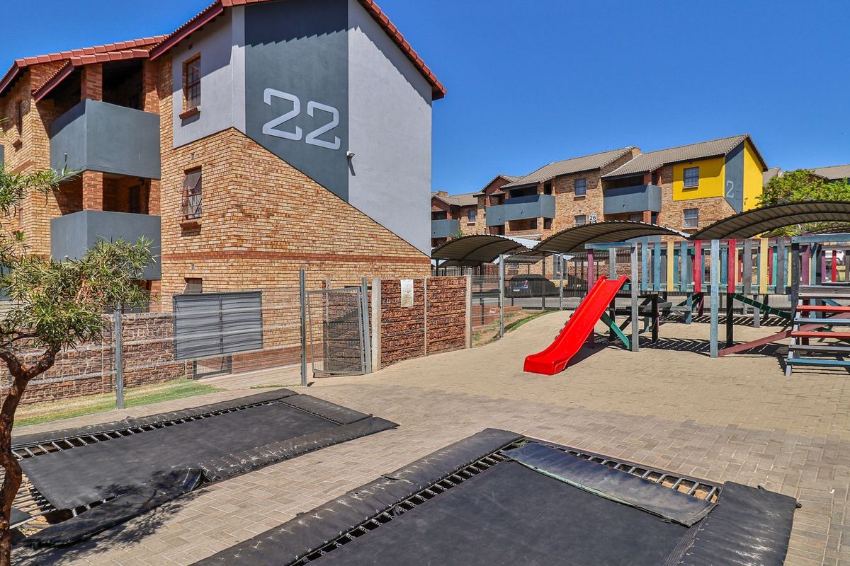 Exterior view of an apartment complex featuring a communal courtyard with a playground, in-ground trampolines, and paved recreational areas.