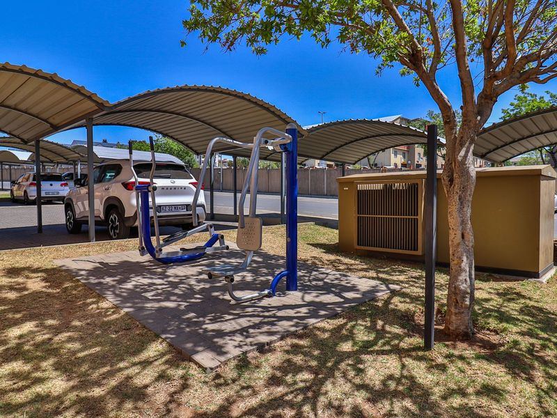 Outdoor gym area featuring fixed exercise equipment situated on a paved surface within a residential complex parking area.