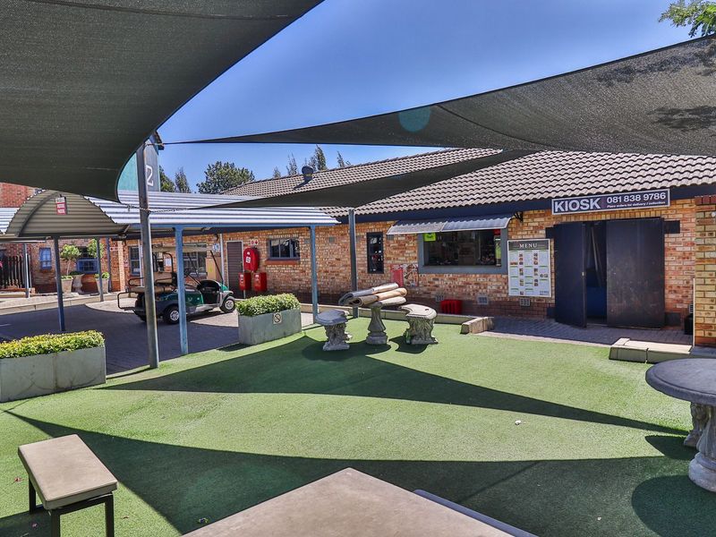 A communal outdoor courtyard area featuring artificial turf, shade sails, and brick building facades with a kiosk service window.