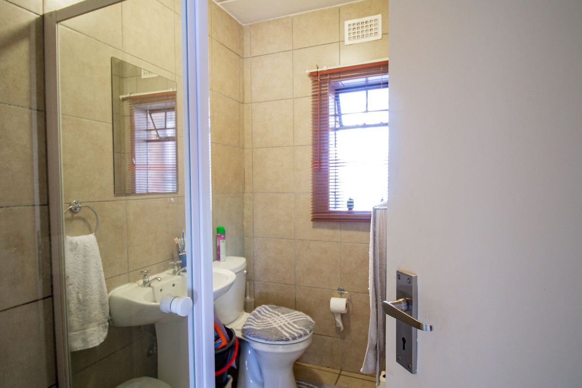 A compact bathroom featuring a pedestal basin, a shower enclosure, and neutral wall tiling, offering a functional layout with natural light from the window.