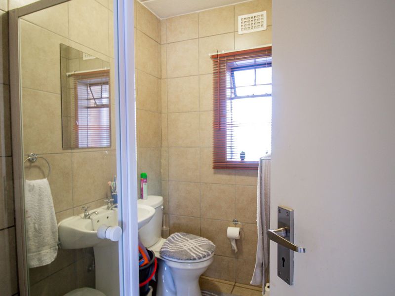 A compact bathroom featuring a pedestal basin, a shower enclosure, and neutral wall tiling, offering a functional layout with natural light from the window.