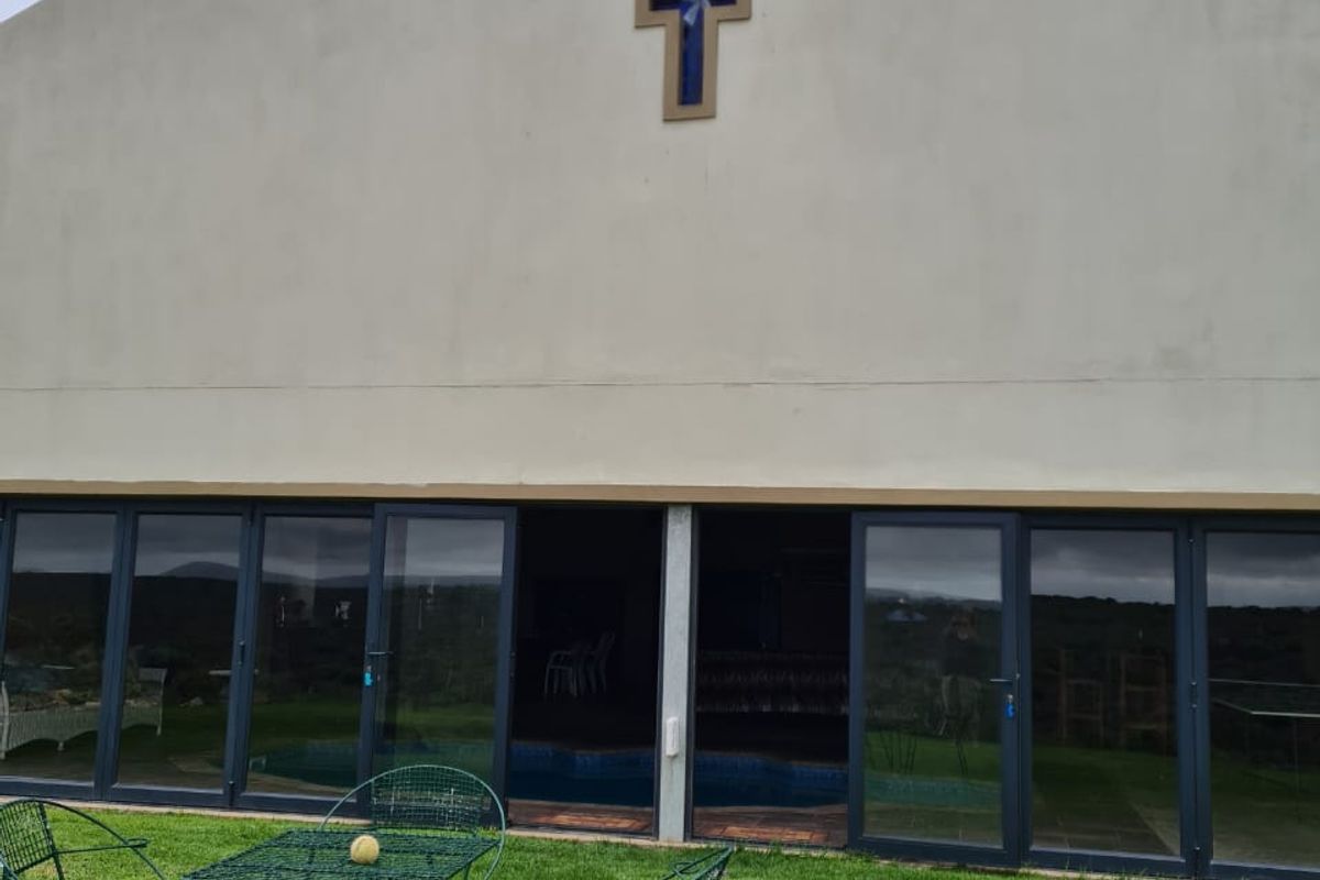 Rear view of the property featuring a large plastered facade with a decorative cross and extensive glass sliding doors opening onto the garden.