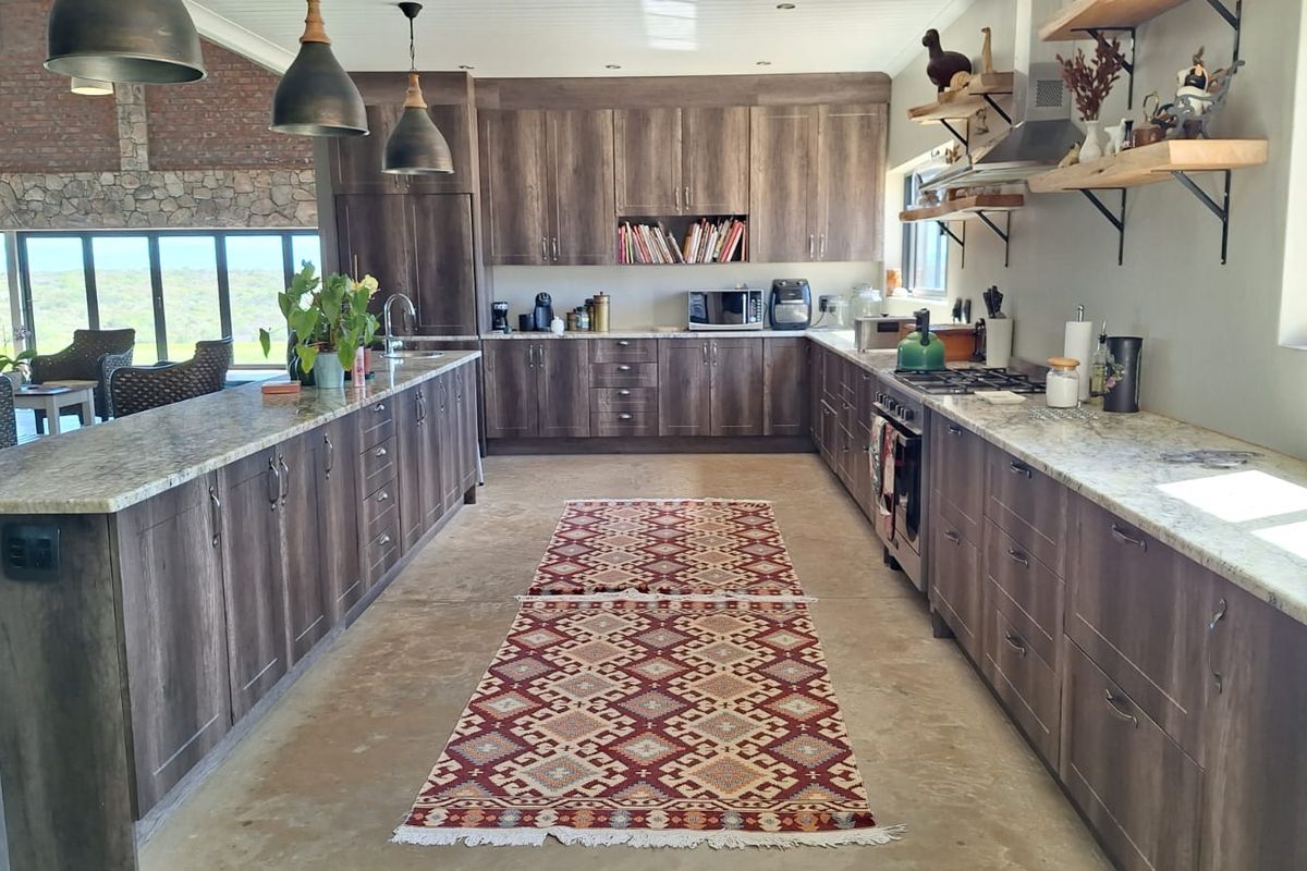 Spacious modern kitchen featuring dark wood cabinetry, granite countertops, gas hob, and integrated appliances, with an open-plan layout overlooking the surrounding landscape.