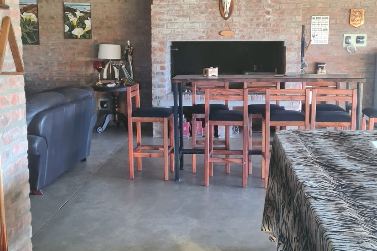 Spacious living area featuring rustic exposed brick walls, stone masonry accents, a large built-in fireplace, and polished concrete flooring under exposed timber beams.
