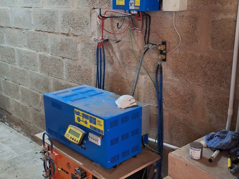 Utility area featuring a solar power system with inverter, charge controller, and battery bank mounted against an unfinished concrete block wall.