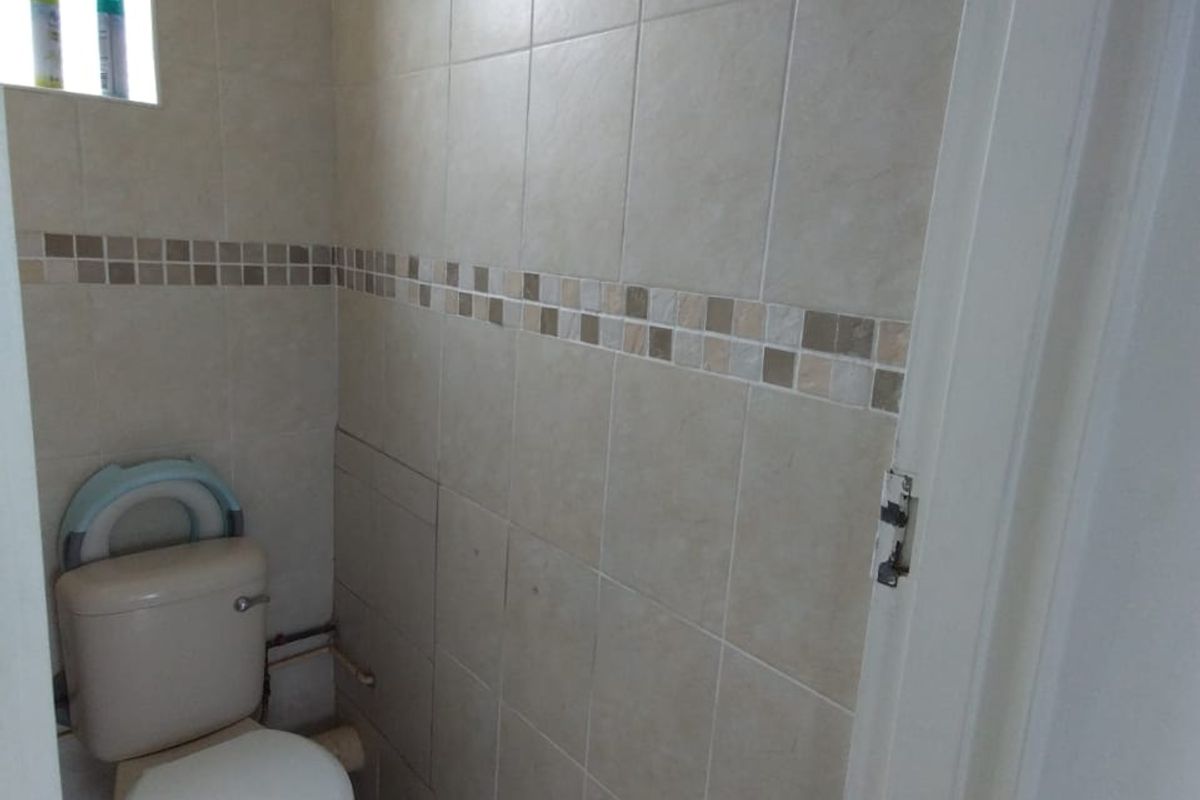 A compact guest toilet featuring neutral wall and floor tiling with a decorative mosaic border and a window for natural ventilation.