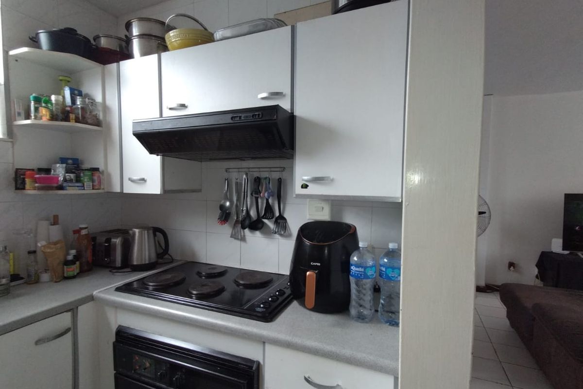 Compact kitchen featuring white cabinetry, a built-in electric hob, oven, and extractor fan, with tiled splashbacks and open shelving.