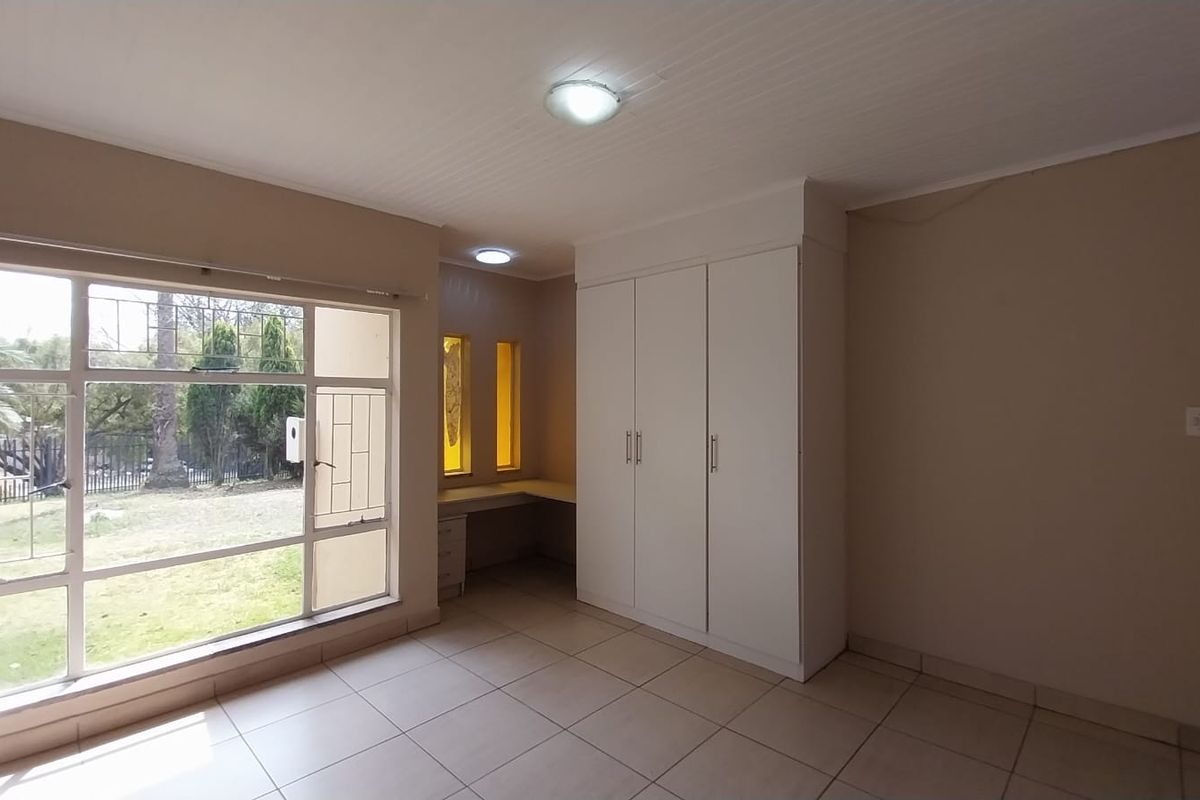 A bright bedroom featuring large windows, built-in wardrobes, and a dedicated built-in desk area with tiled flooring.