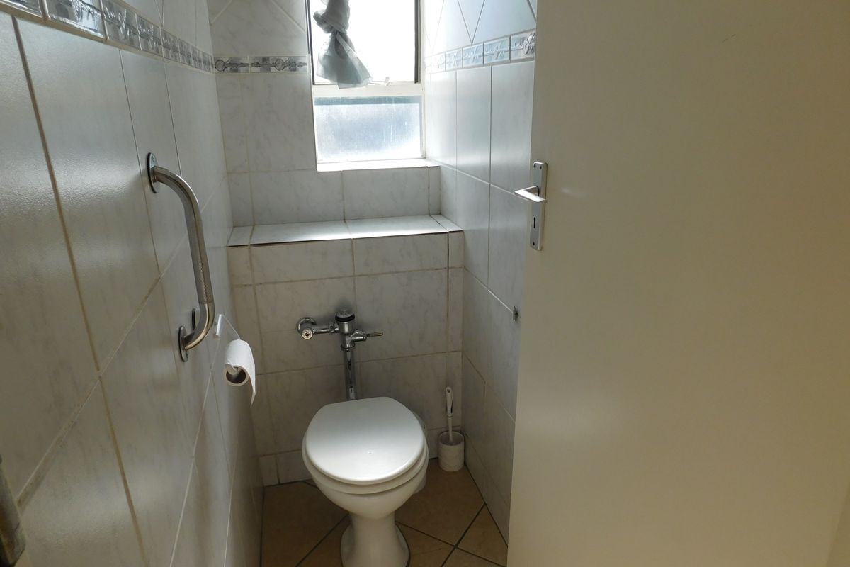 A compact bathroom featuring tiled walls and flooring, equipped with a toilet and a safety grab rail.