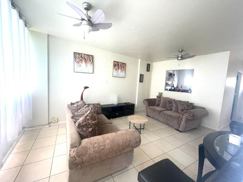 Spacious living room featuring neutral tiled flooring, dual ceiling fans, and a convenient pass-through window connecting to the kitchen area.