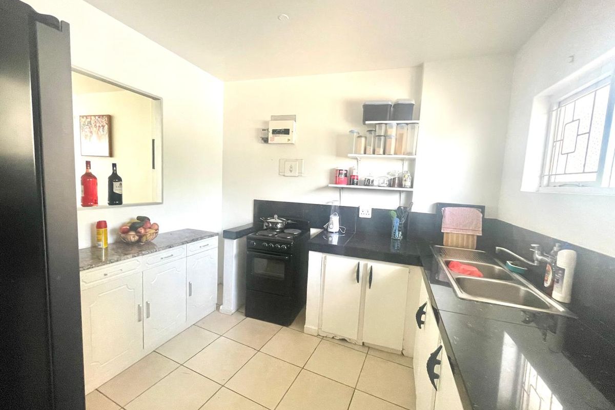 A functional kitchen featuring white cabinetry, dark granite countertops, a double basin sink, and a freestanding stove with tiled flooring.