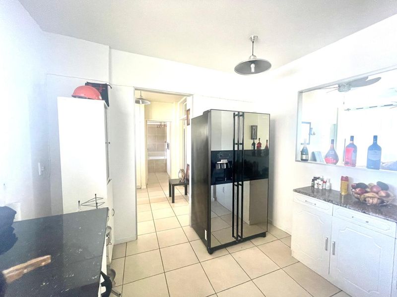 A functional kitchen area featuring tiled flooring, built-in cabinetry with stone countertops, and a decorative mirrored wall section.