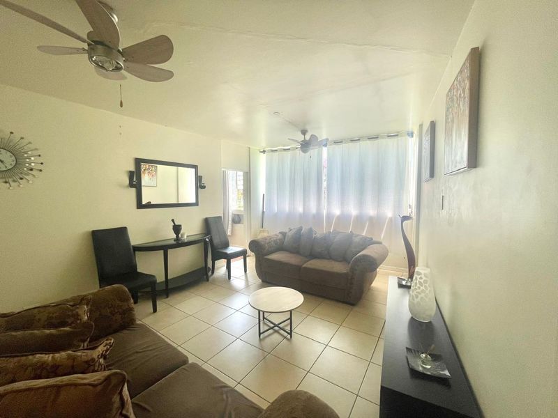 A living room featuring ceramic tile flooring, ceiling fans, and a sliding glass door providing natural light.