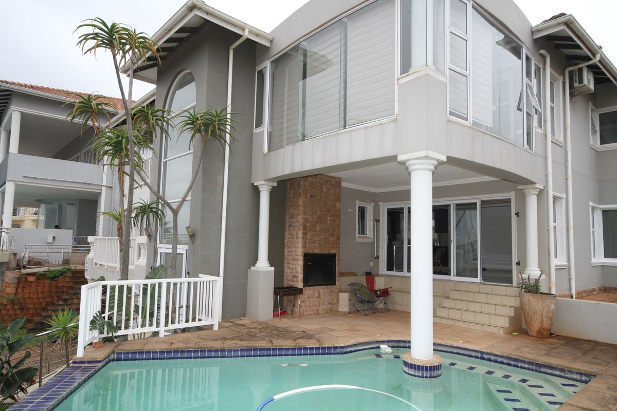 Rear exterior view featuring a swimming pool, covered patio with a built-in braai, and a multi-level facade with large glass windows.