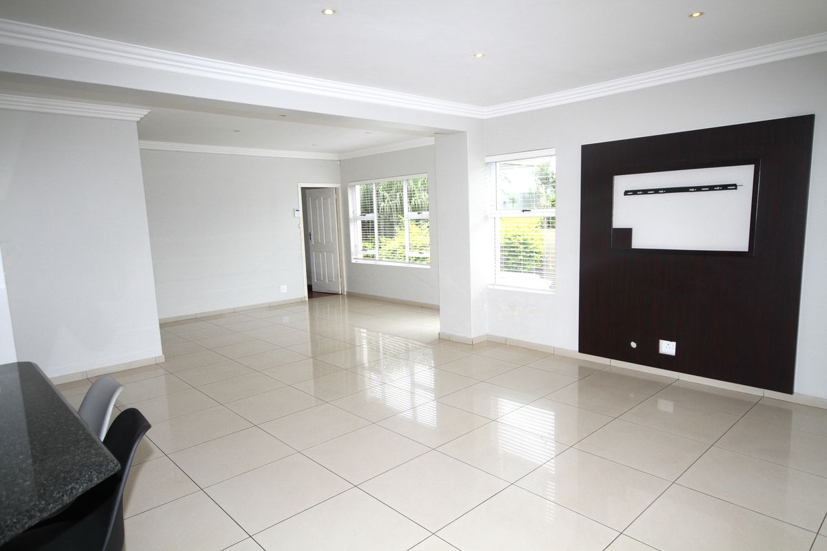 Spacious, open-plan living area featuring polished porcelain floor tiles, recessed downlighting, crown molding, and a modern built-in media wall unit.