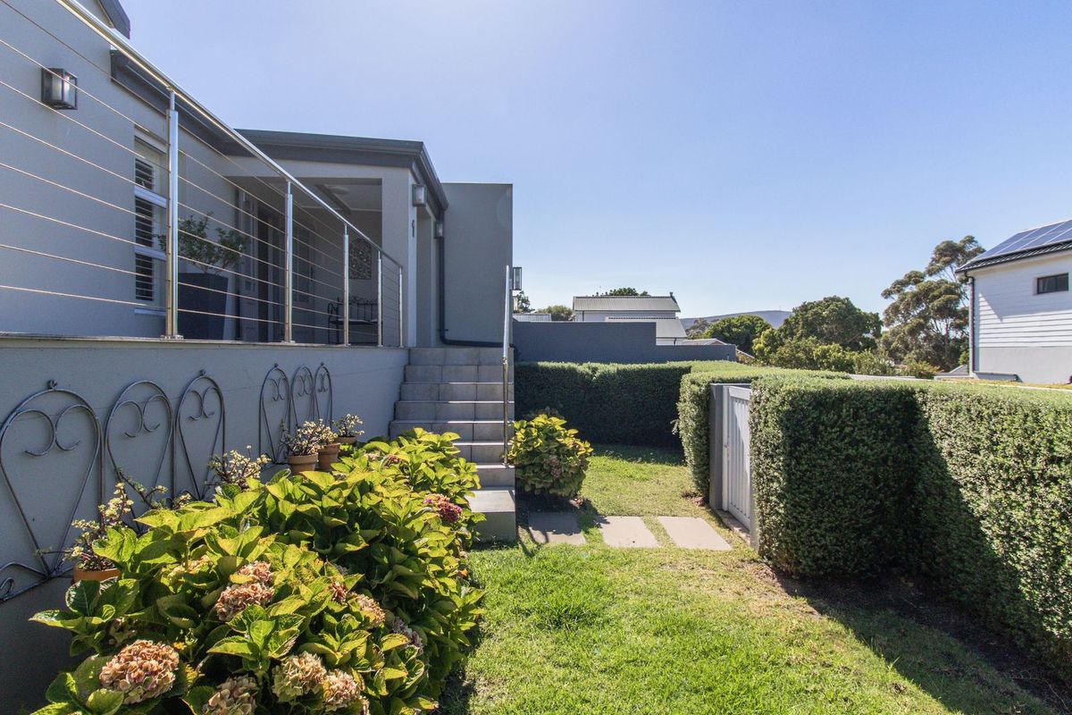 A well-maintained rear garden featuring a manicured hedge, lawn, concrete steps, and a modern elevated patio with a stainless steel balustrade.