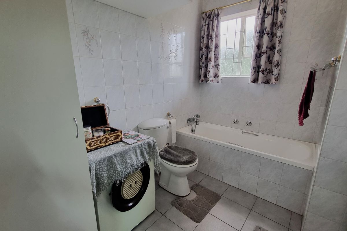A functional bathroom featuring a built-in bathtub, toilet, and tiled finishes throughout, offering a clean and practical space.