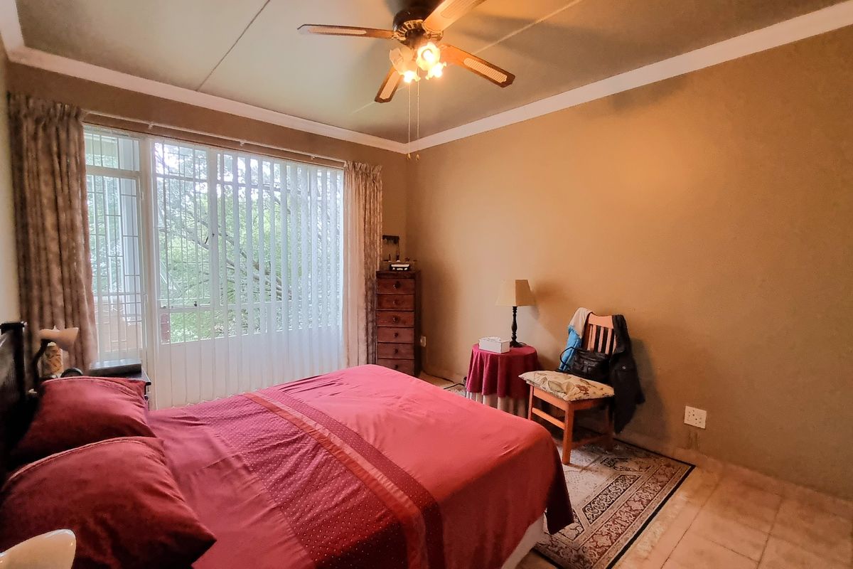 A bedroom featuring tiled flooring, a ceiling fan, and large windows with security gates, offering a functional space with potential for cosmetic updates.