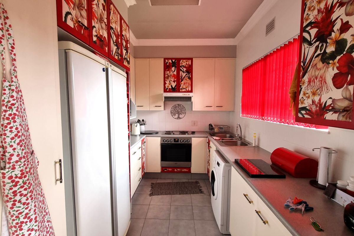 A functional galley-style kitchen featuring built-in cabinetry, an integrated oven and hob, and a double stainless steel sink with tiled flooring.