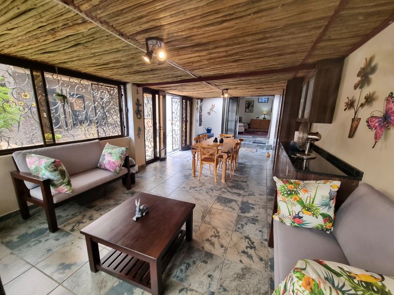 A spacious covered patio featuring a rustic thatched ceiling, tiled flooring, and built-in cabinetry with granite countertops, providing a versatile indoor-outdoor entertainment area.
