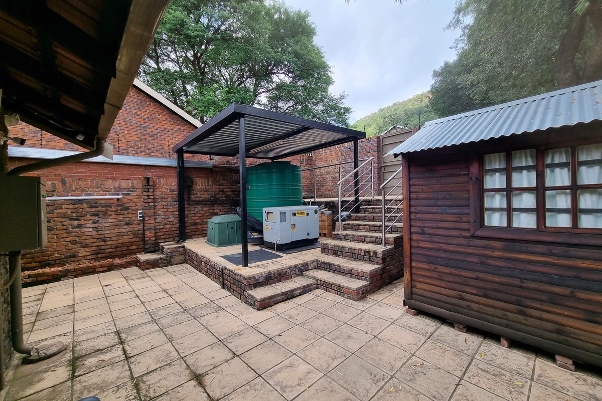 Rear courtyard area featuring brick paving, a covered utility space with a water tank and generator, and a timber storage shed.