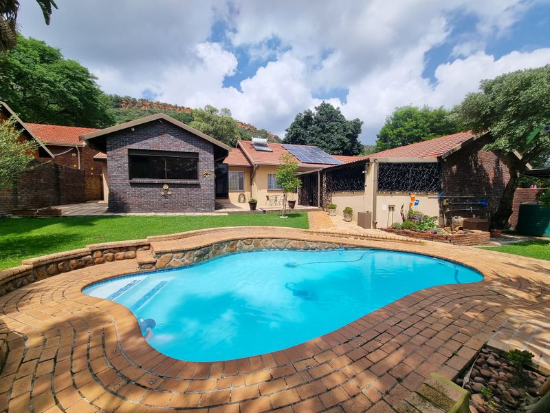 A well-maintained rear garden featuring a swimming pool with brick paving, solar panels, and a mix of brick and plastered exterior finishes.