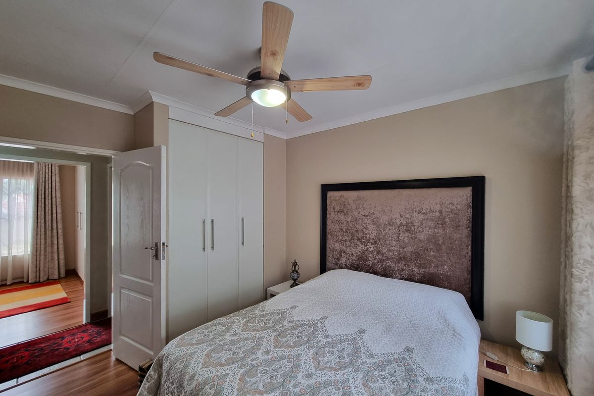 A well-maintained bedroom featuring built-in wardrobes, a ceiling fan, and laminate flooring, with a view into the adjacent hallway.