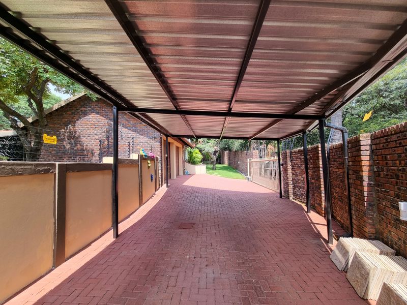 A spacious paved driveway featuring a covered metal carport structure, enclosed by brick perimeter walls and secure fencing.