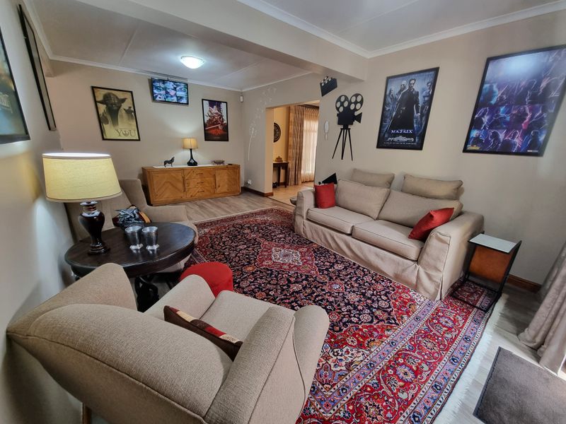 A comfortable living room featuring laminate flooring and cove cornice, with an open transition to an adjacent room.