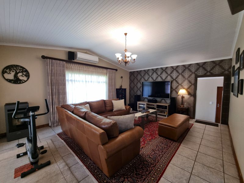 Spacious living room featuring tiled flooring, a tongue and groove ceiling, feature wallpaper, and a wall-mounted air conditioning unit.