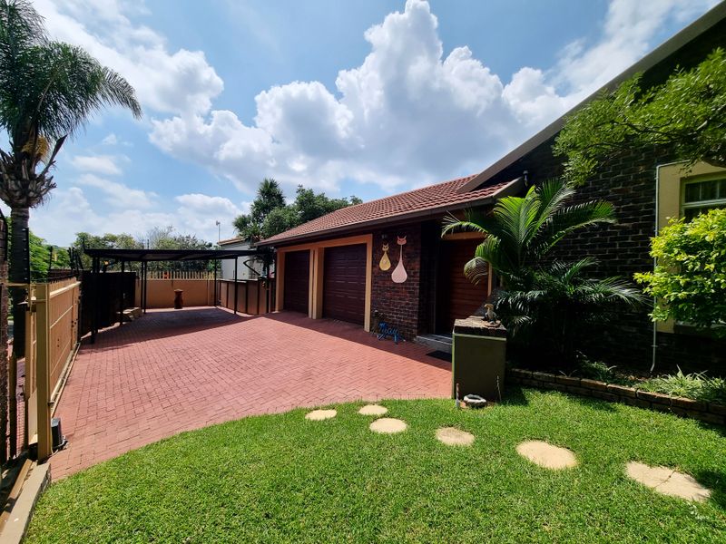 Front exterior view featuring a paved driveway, double garage, carport, and well-maintained garden area with facebrick facade.
