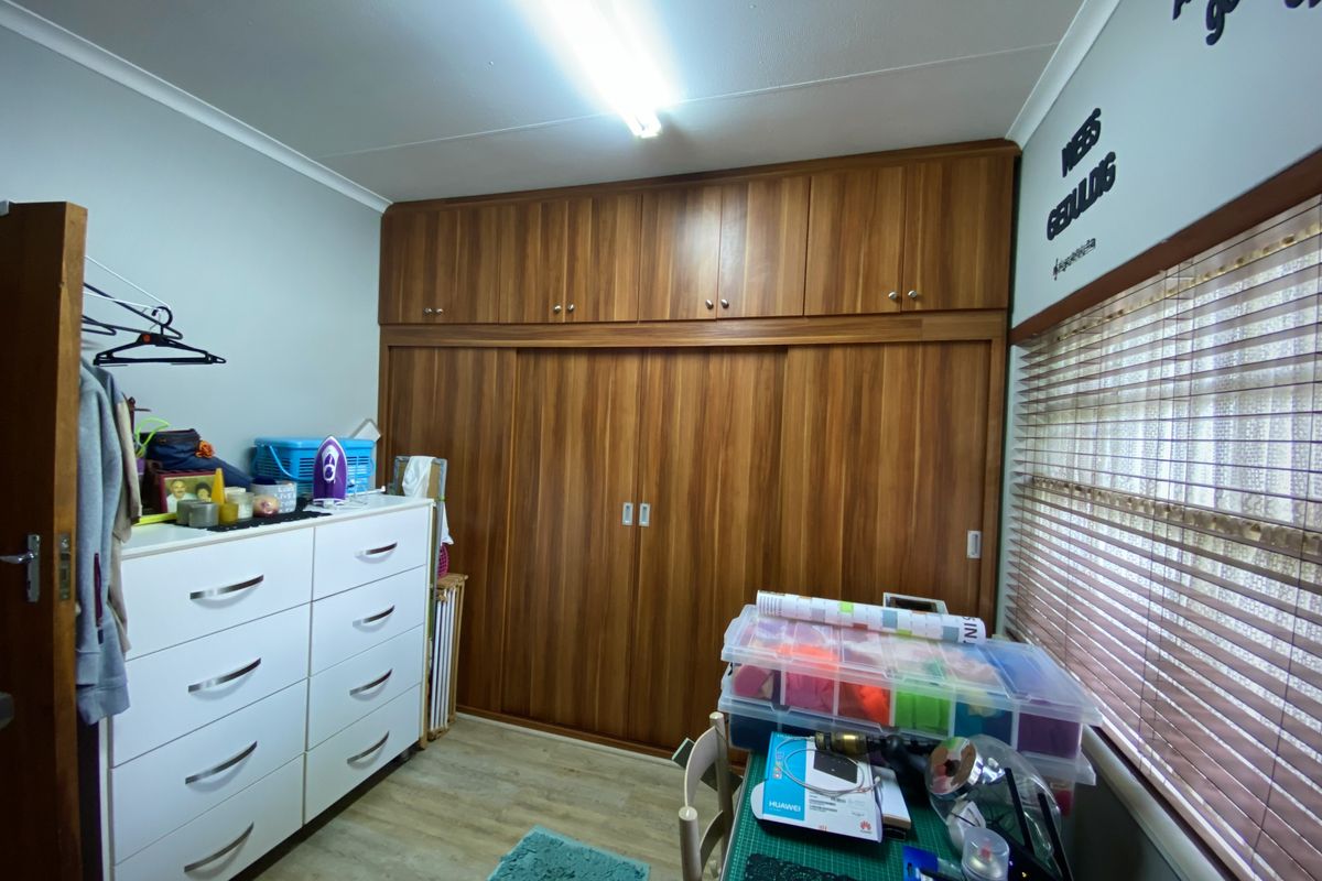 A bedroom featuring extensive floor-to-ceiling wood-finish built-in cupboards and venetian blinds, providing ample storage and natural light control.