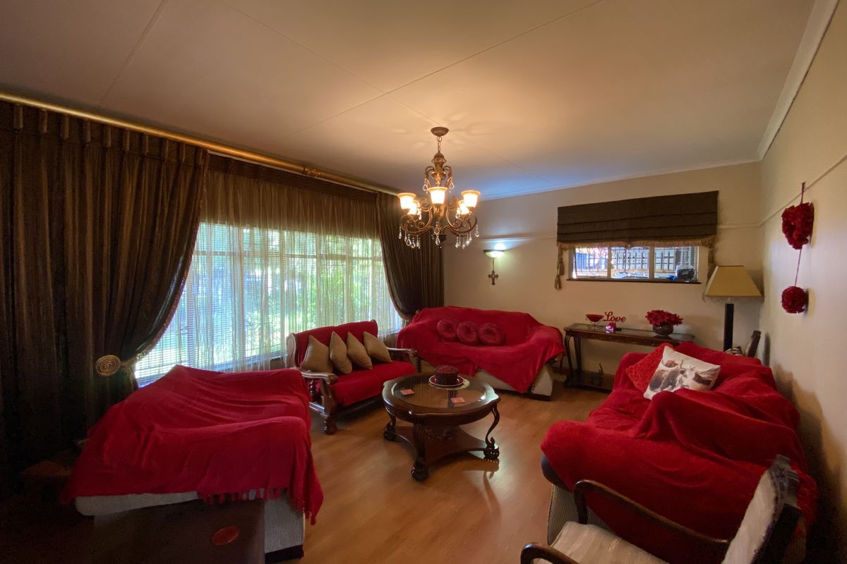 A spacious living room featuring laminate flooring, a decorative chandelier, and large windows with curtain rails and blinds.