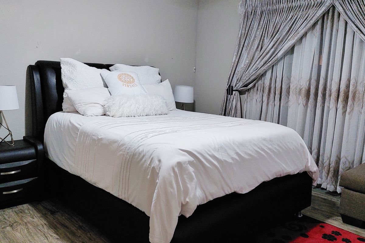 A bedroom featuring laminate flooring and full-length window curtains.