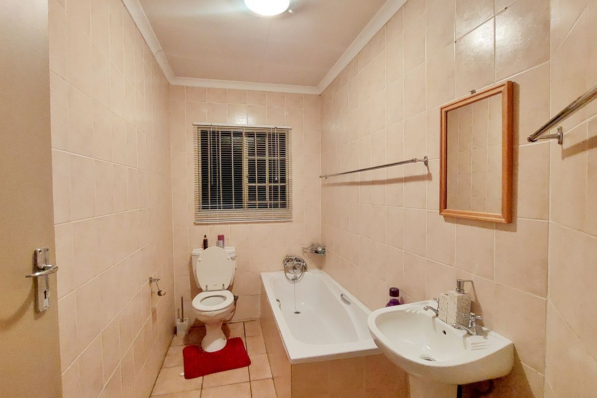 A functional bathroom featuring a bathtub, pedestal basin, and toilet, finished with neutral wall and floor tiles.