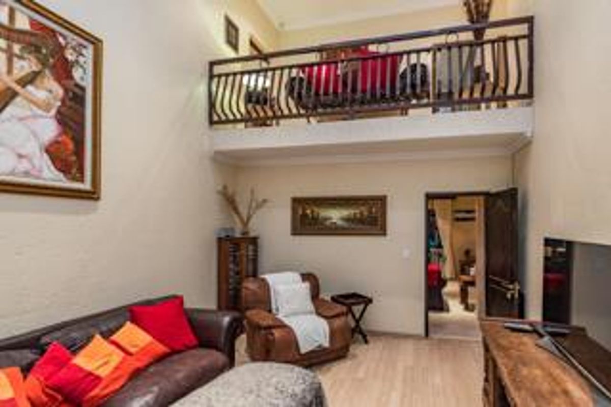 A double-volume living area featuring a mezzanine level with a decorative metal railing, providing an open and airy feel to the space.