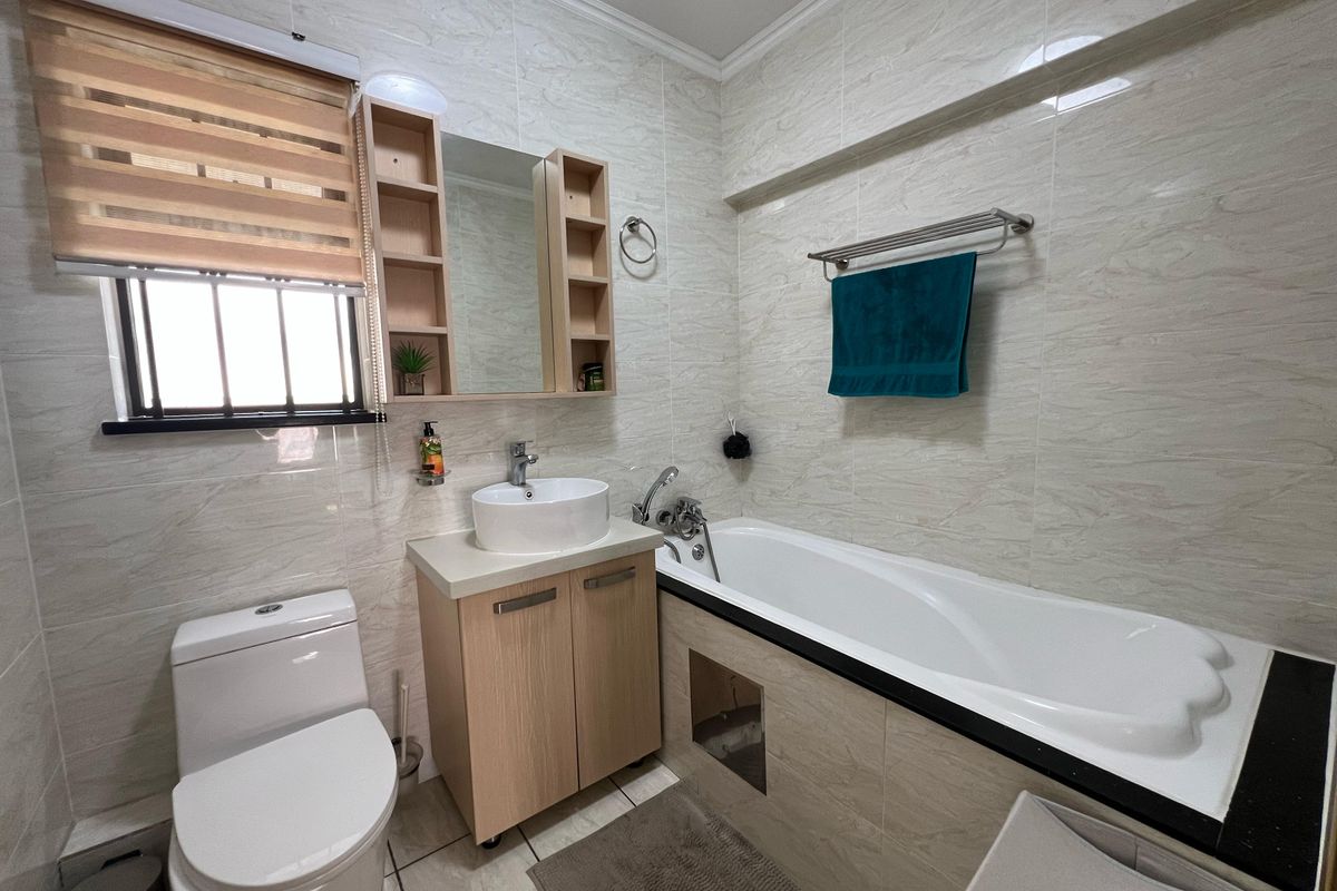 A functional bathroom featuring a vessel sink vanity, bathtub with tiled surround, and wall-mounted towel rail, finished with neutral marble-effect wall tiles.
