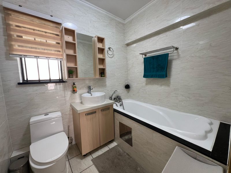 A functional bathroom featuring a vessel sink vanity, bathtub with tiled surround, and wall-mounted towel rail, finished with neutral marble-effect wall tiles.